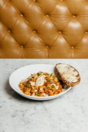 Closeup of pasta dish and toasted slice of bread resting on the edge of bowl