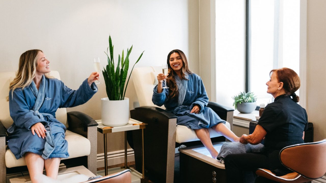Two women in robes with champagne getting pedicures