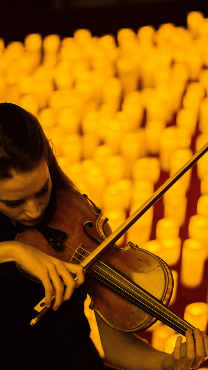 woman playing violin in front of lit candles