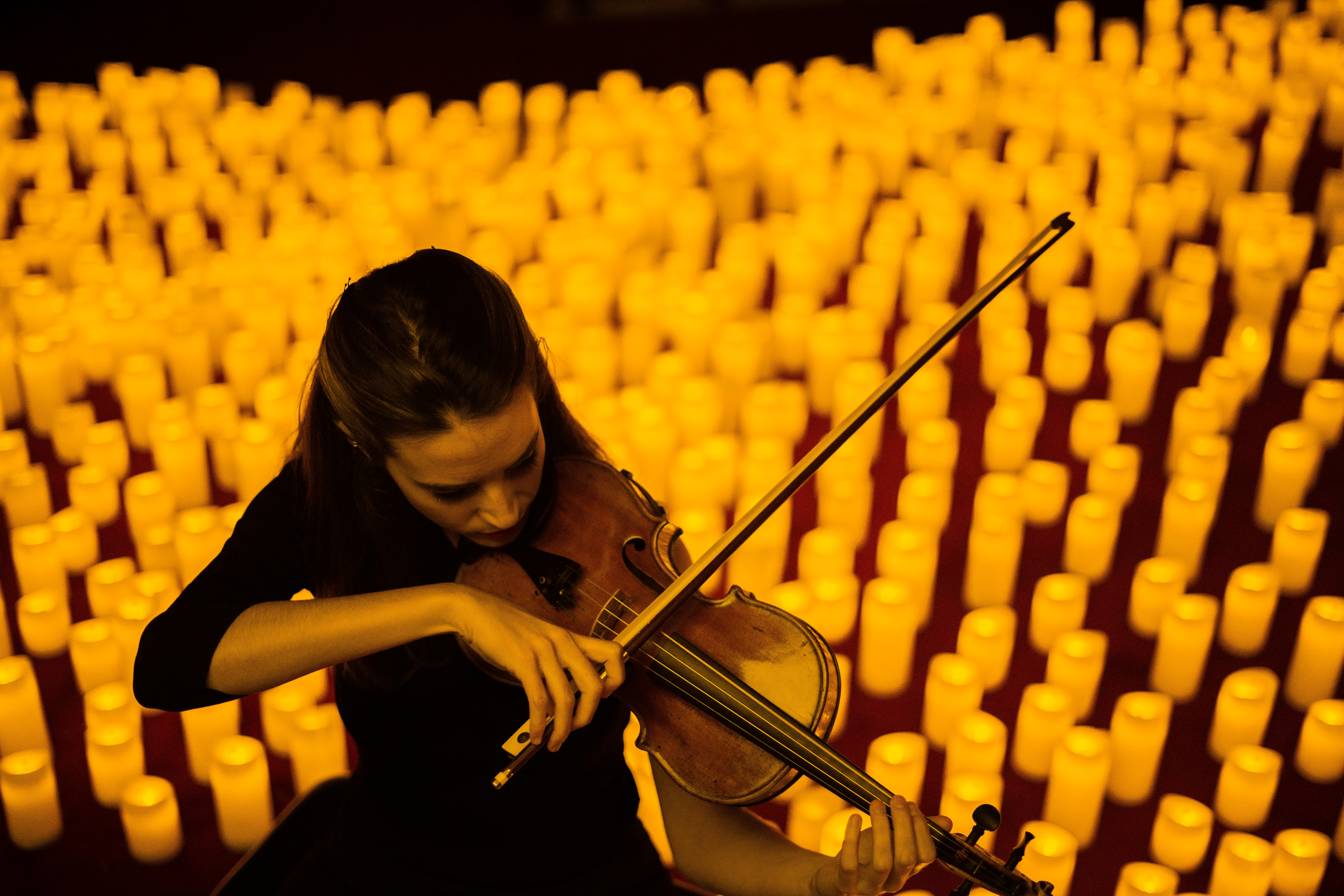 woman playing violin in front of lit candles