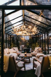 Inside of glass chalet house featuring an antler chandelier, cozy lounge furniture, fur rungs and vintage lanterns