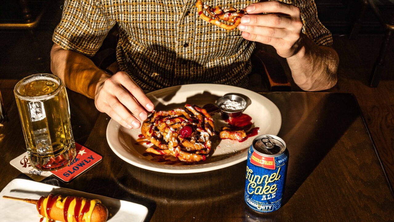 Man eating funnel cake with beer and a corndog nearby