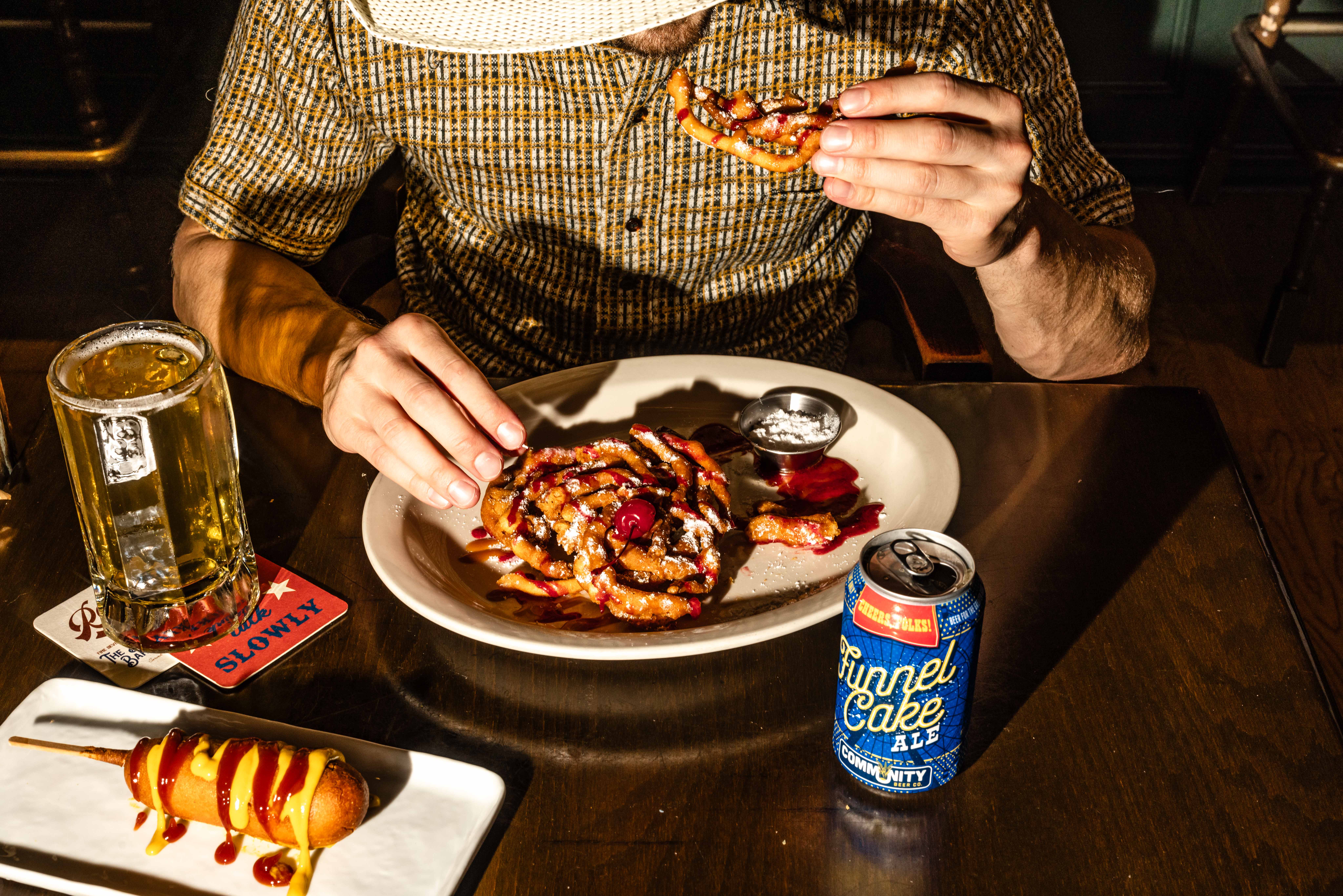 Man eating funnel cake with beer and a corndog nearby