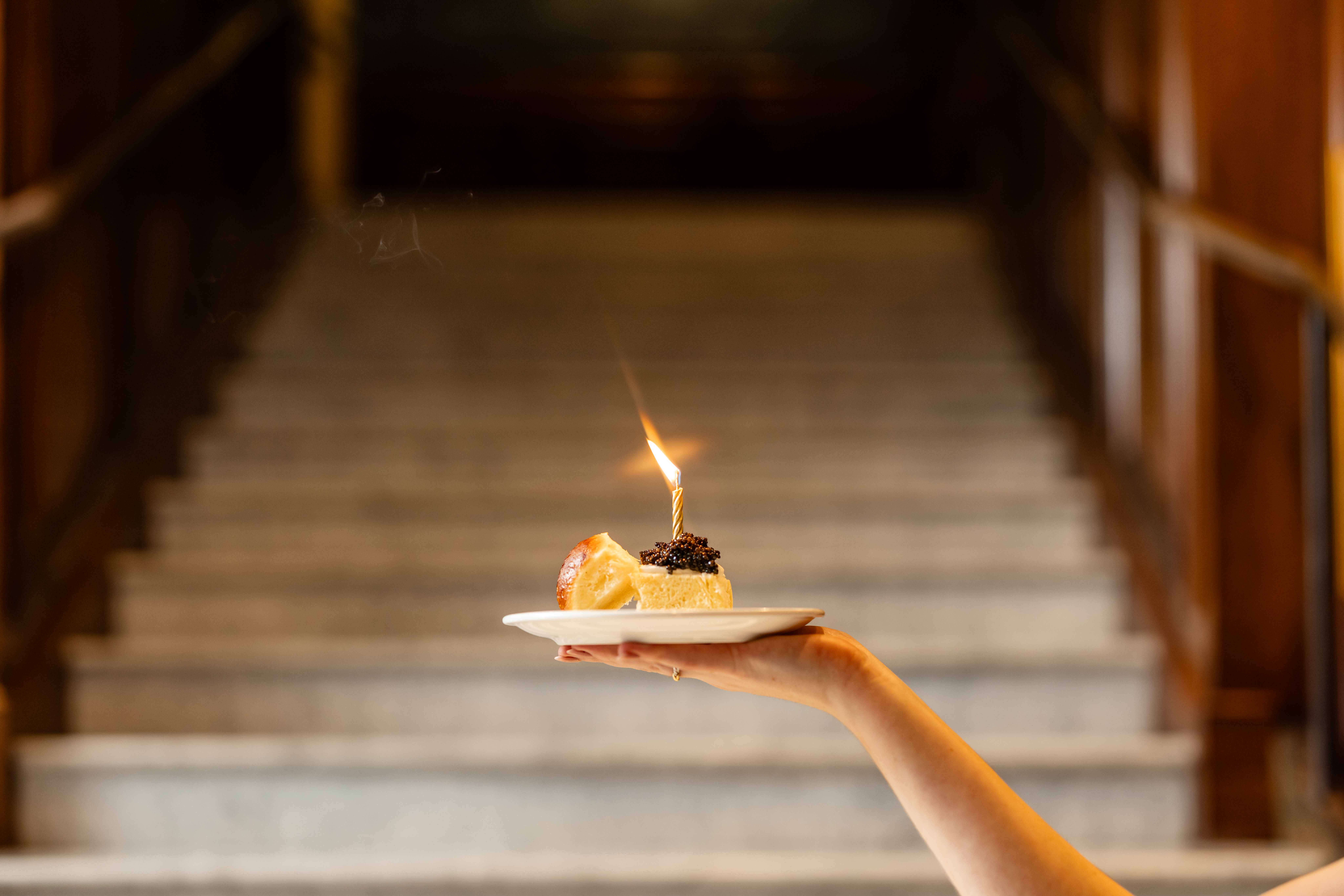 Caviar slider on a plate with a lit candle in front of the staircase